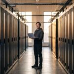 Technicus met laptop in een gang van een datacenter met serverracks, symbool voor beveiligde blockchain-infrastructuur