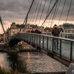 Anoniem persoon op een moderne stalen brug over een rivier in de schemering, als beeld bij de discussie over crypto-bruggen