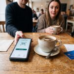 Smartphone met een betaal-app op een cafétafel naast een kopje koffie en een betaalkaart