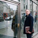 Ondernemer met een map papieren staat voor de dichte glazen deur van een bank in Londen