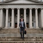 Een persoon loopt de trappen op van een Amerikaans justitiegebouw met hoge stenen zuilen