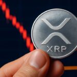 Fysieke XRP-munt voor een scherm met een dalende koersgrafiek die een steunlijn nadert