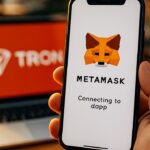 Smartphone met MetaMask-logo dat verbinding maakt, met het TRON-logo op een laptopscherm op de achtergrond